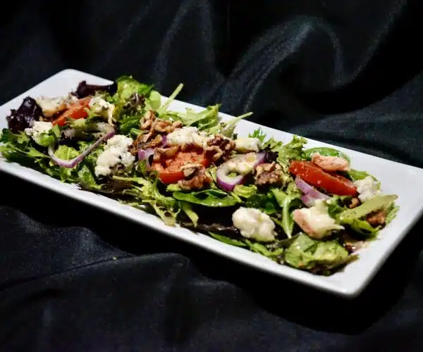 white plate with mix greens, sliced tomatoes, gorgonzola, walnuts
